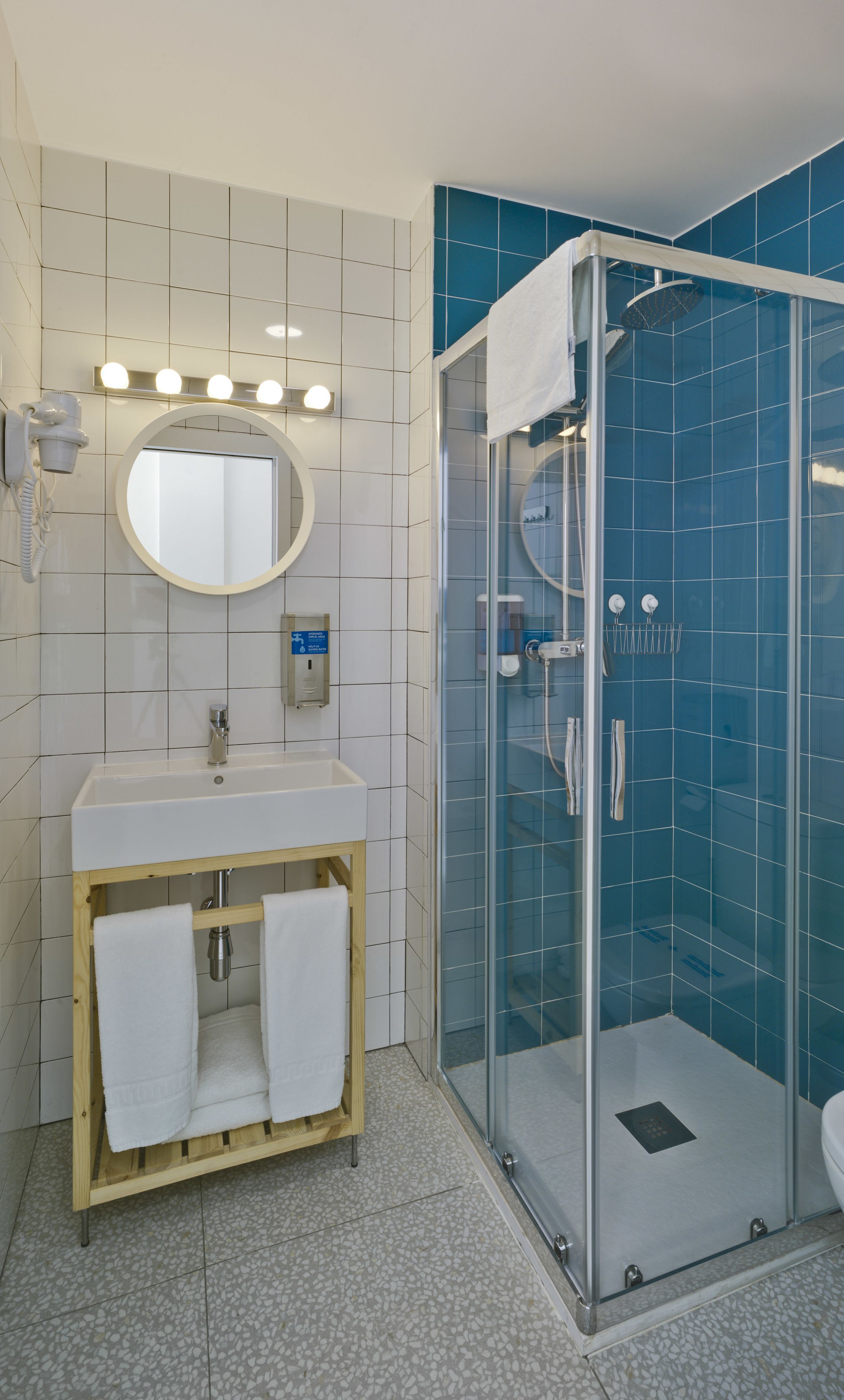 Une salle de bain moderne avec un lavabo blanc, un miroir et un meuble-lavabo, une douche en verre et un sol carrelé.