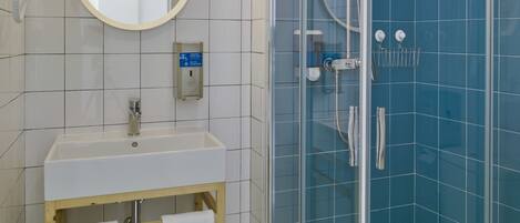 Une salle de bain moderne avec un lavabo blanc, un miroir et un meuble-lavabo, une douche en verre et un sol carrelé.