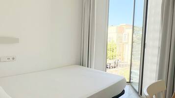Ein Hotelzimmer mit Bett, Tisch und Blick auf Gebäude durch ein großes Fenster.