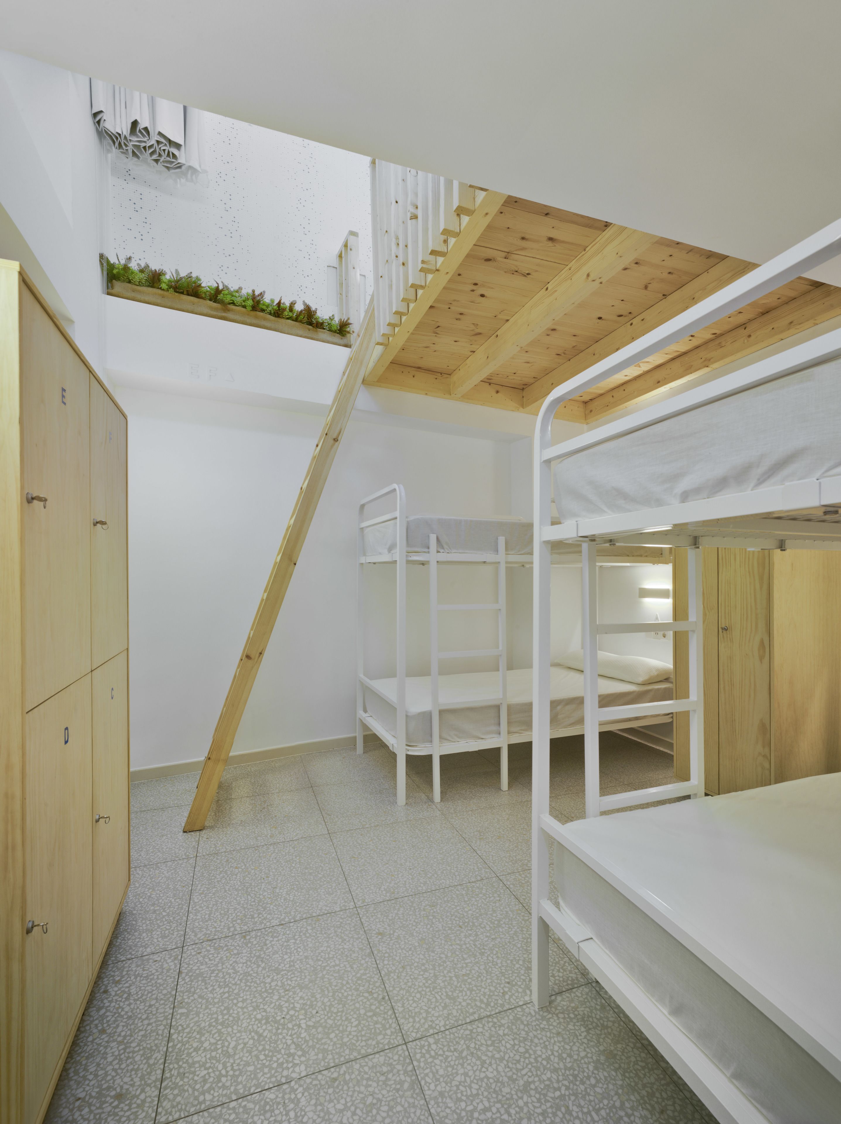 Una habitación con literas, una escalera de madera y un ventanal con vistas a la vegetación.