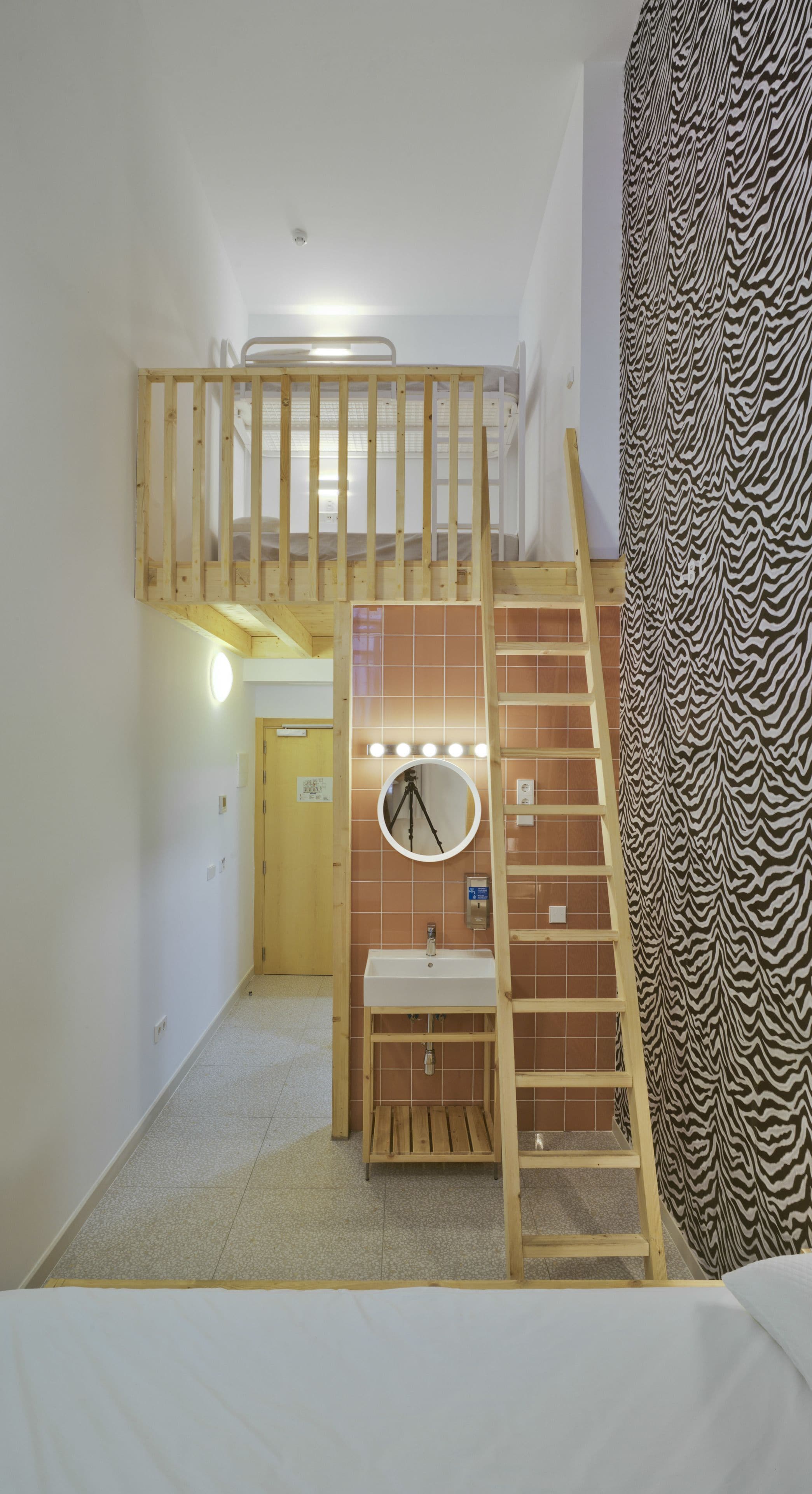 Quarto compacto com uma beliche, banheiro pequeno com espelho e pia, e cortina com padrão de zebra.