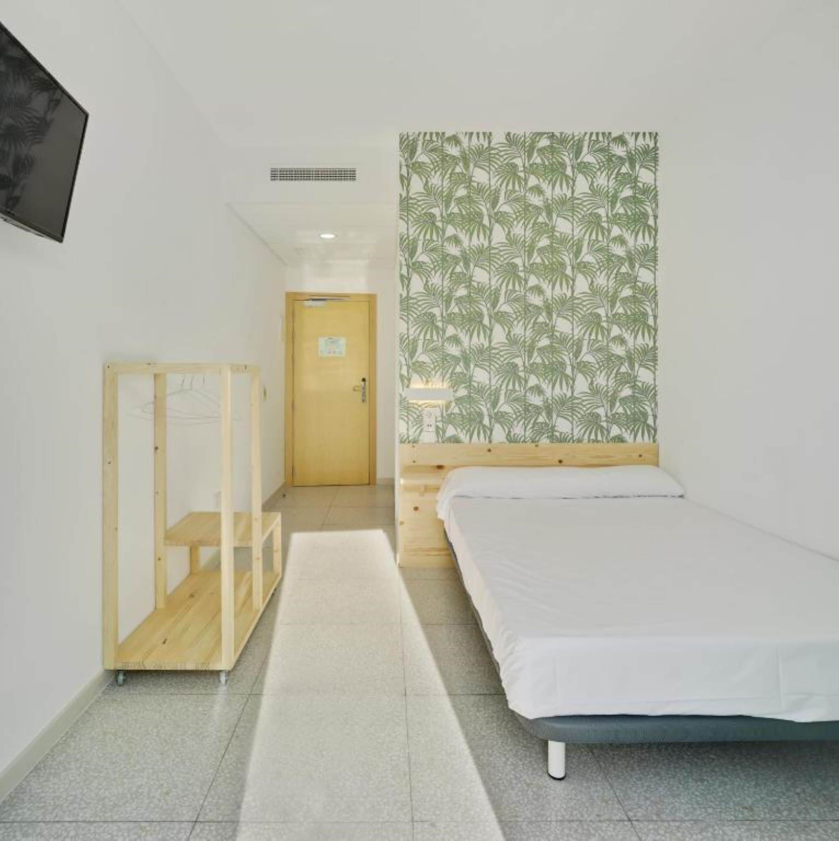 Una camera da letto con un letto, un armadio in legno, una porta e una parete con un motivo a foglia.