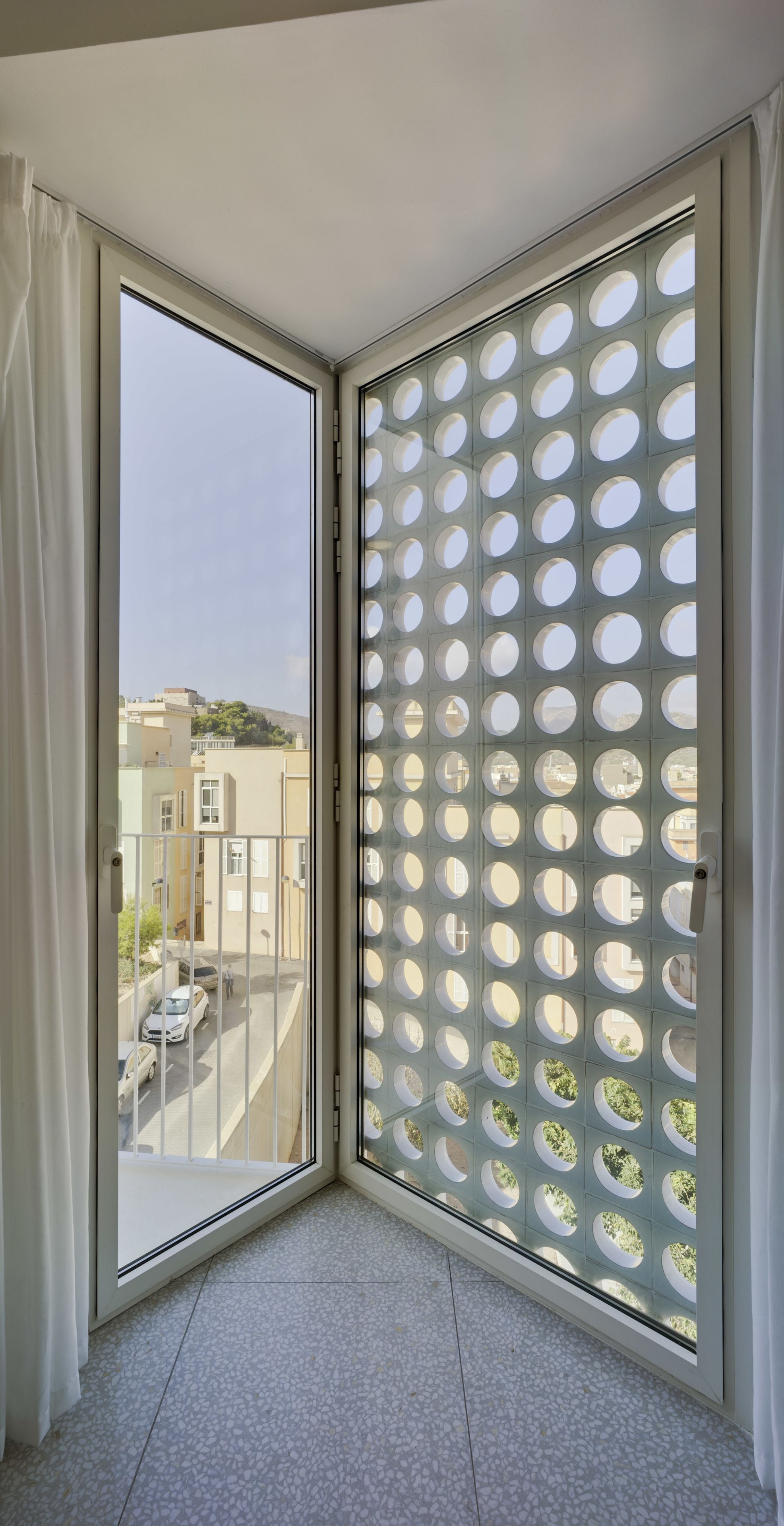 A room with a sliding glass door leading to a balcony with a view of a street and buildings.