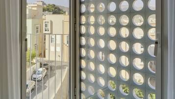 Una habitación con puerta de vidrio corredera que da a un balcón con vista a la calle y edificios.