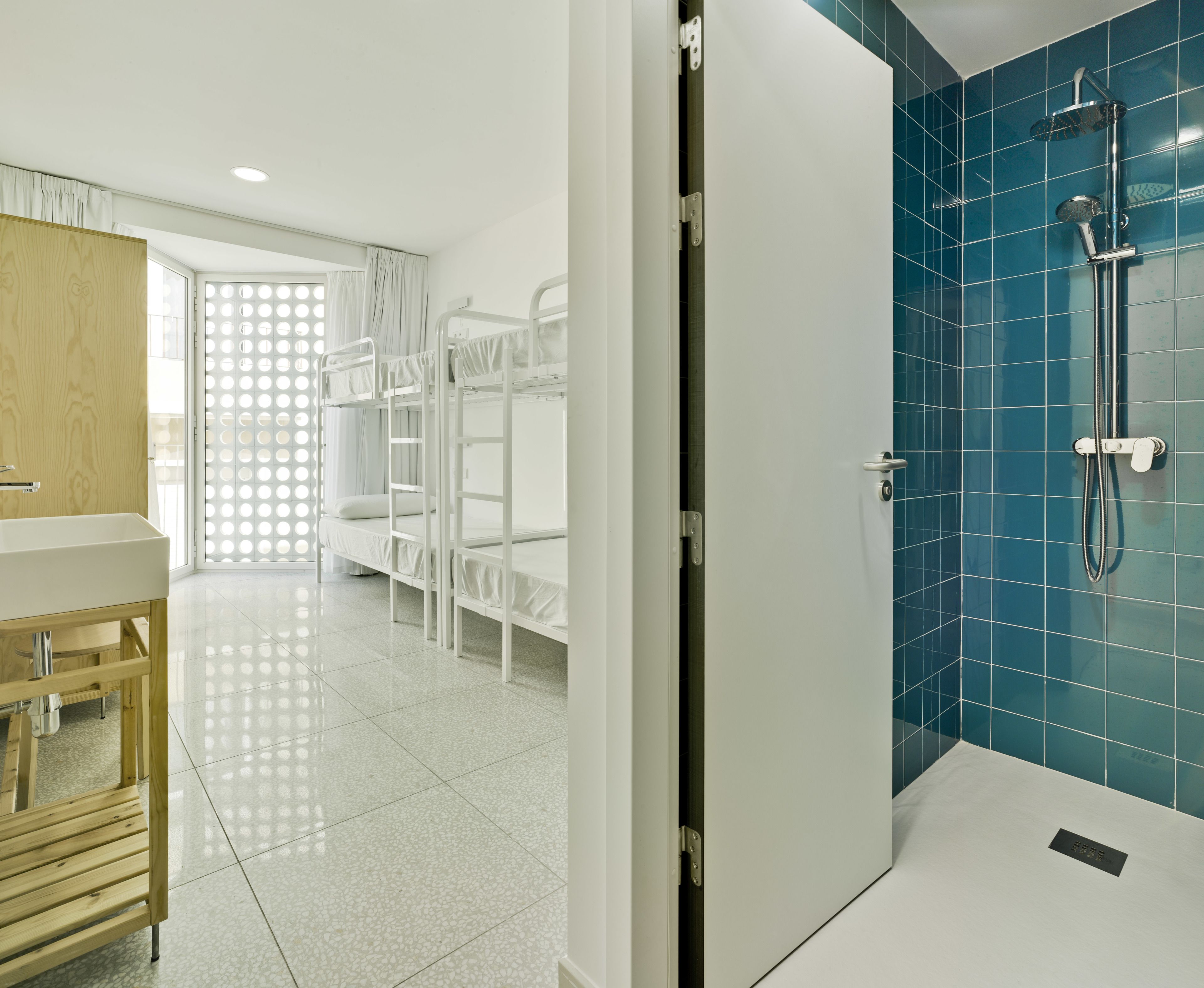 Habitación de hotel con literas, ducha con azulejos azules, tocador de madera y un ventanal con vistas.