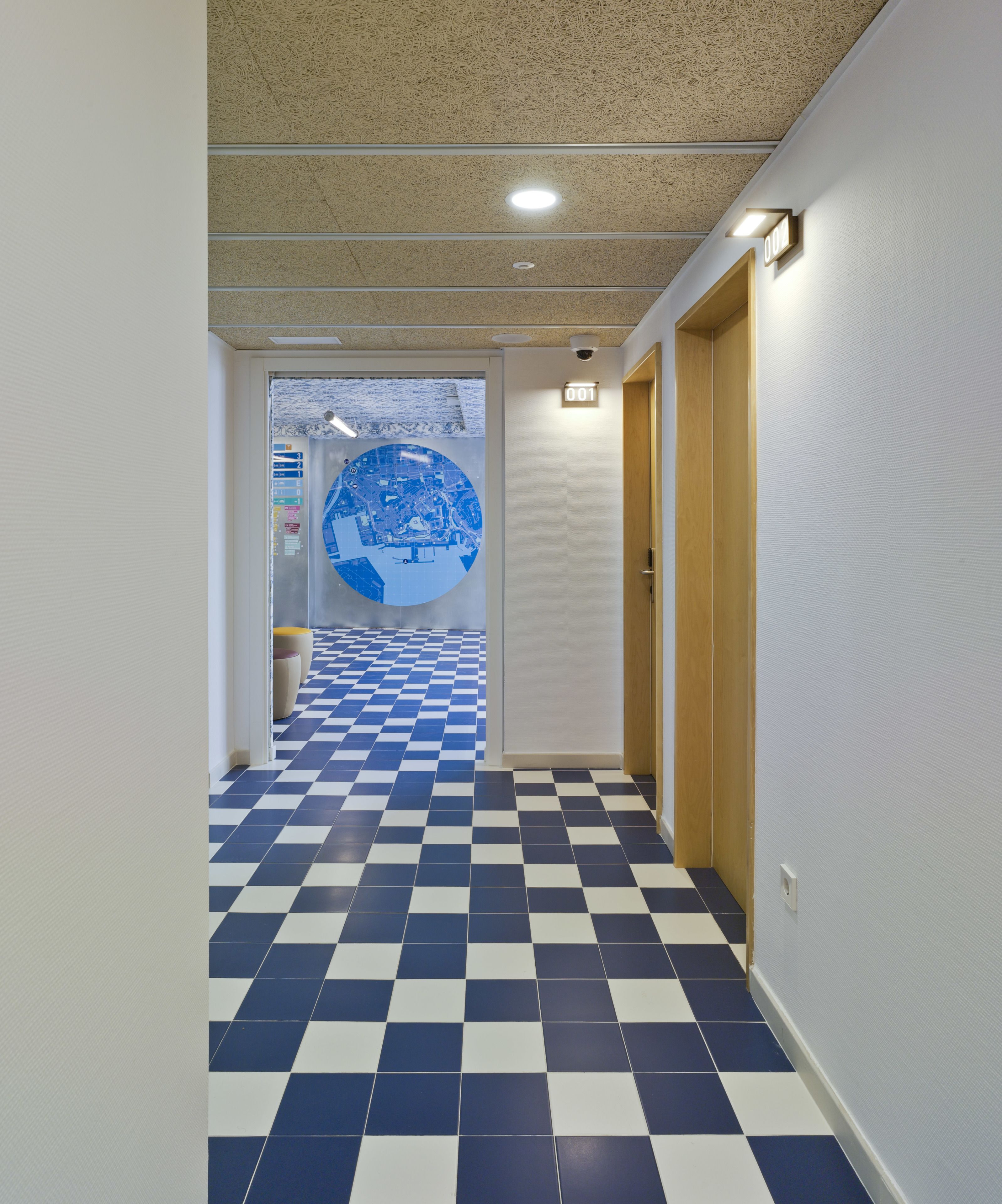 A hallway with a checkered floor pattern, a circular wall decoration, and a door with a number sign.