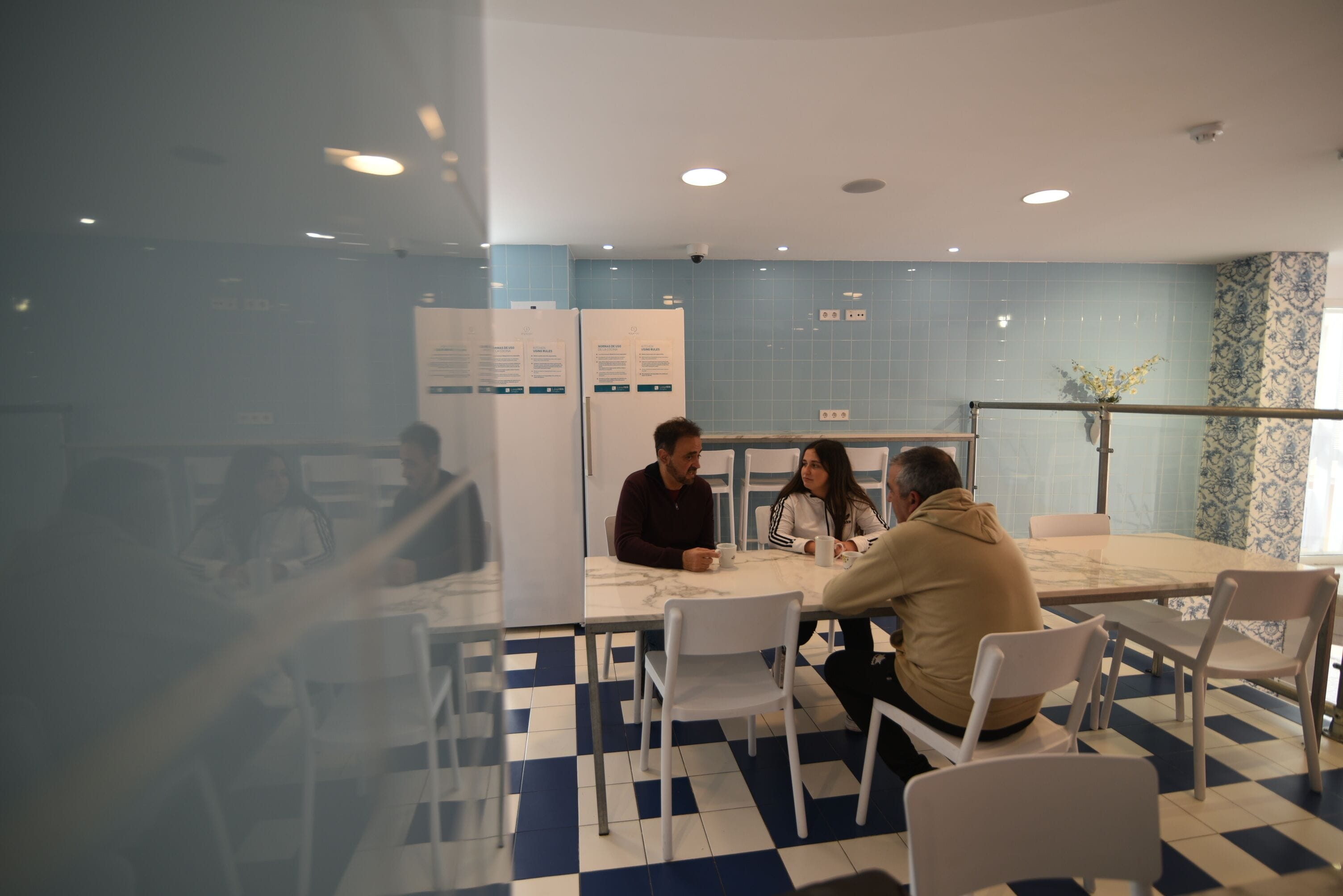 A meeting room with a checkered floor, white chairs, a marble table, and a blue-tiled wall.
