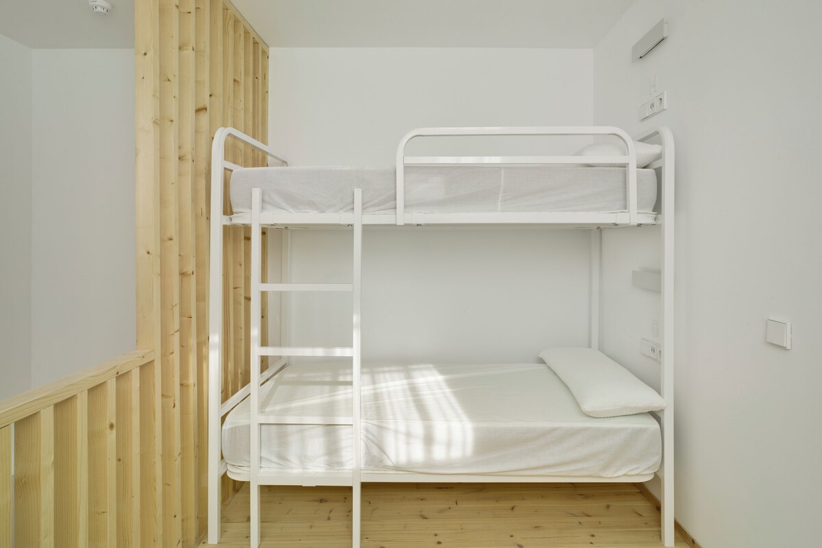 Een stapelbed met een ladder, een houten vloer en een witte muur.