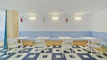 Una habitación con suelo azul y blanco a cuadros, un banco acolchado en tono azul claro y sillas blancas alrededor de una mesa central.