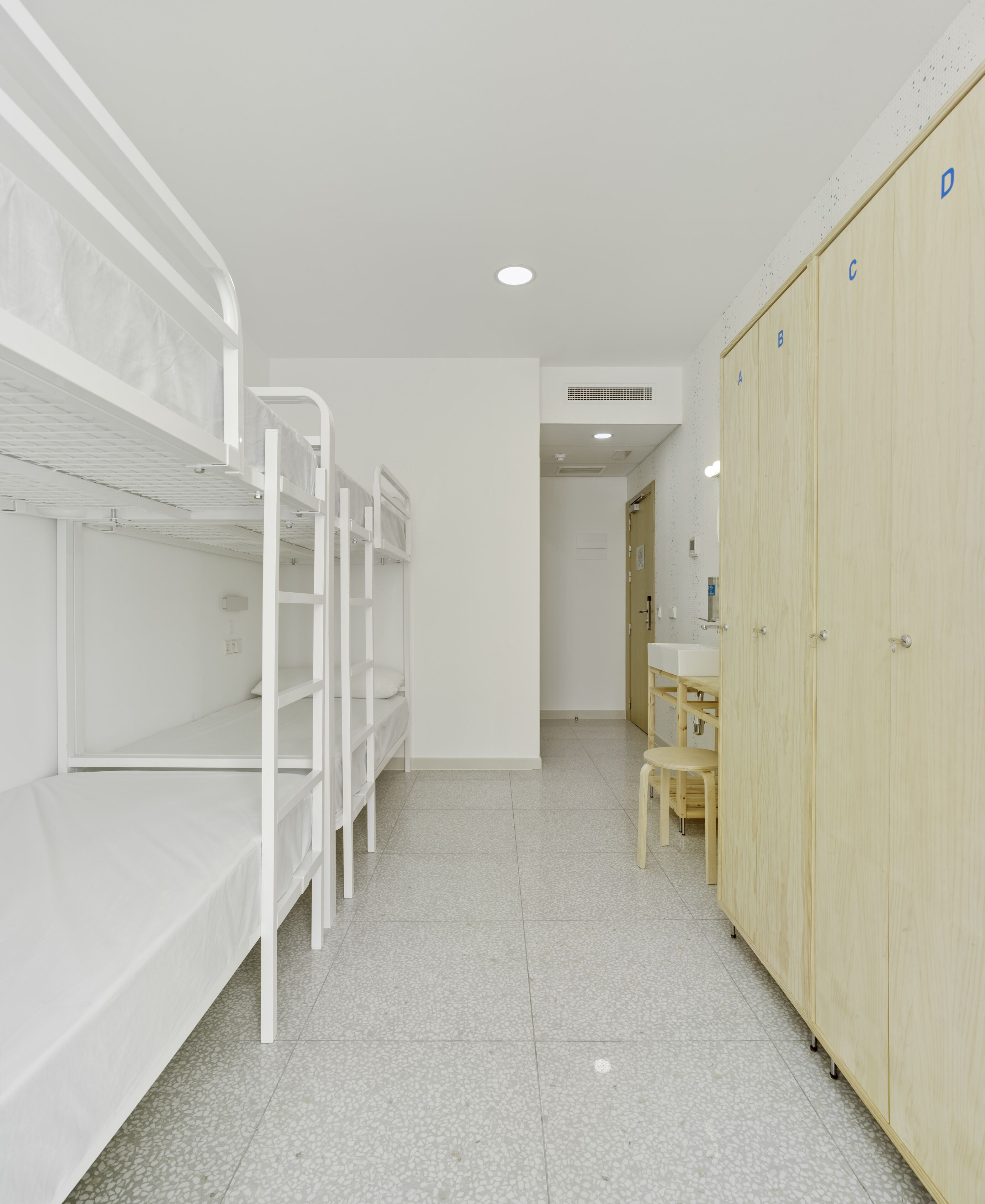 A clean, modern room with bunk beds, a wooden wardrobe, and a small desk with a chair.