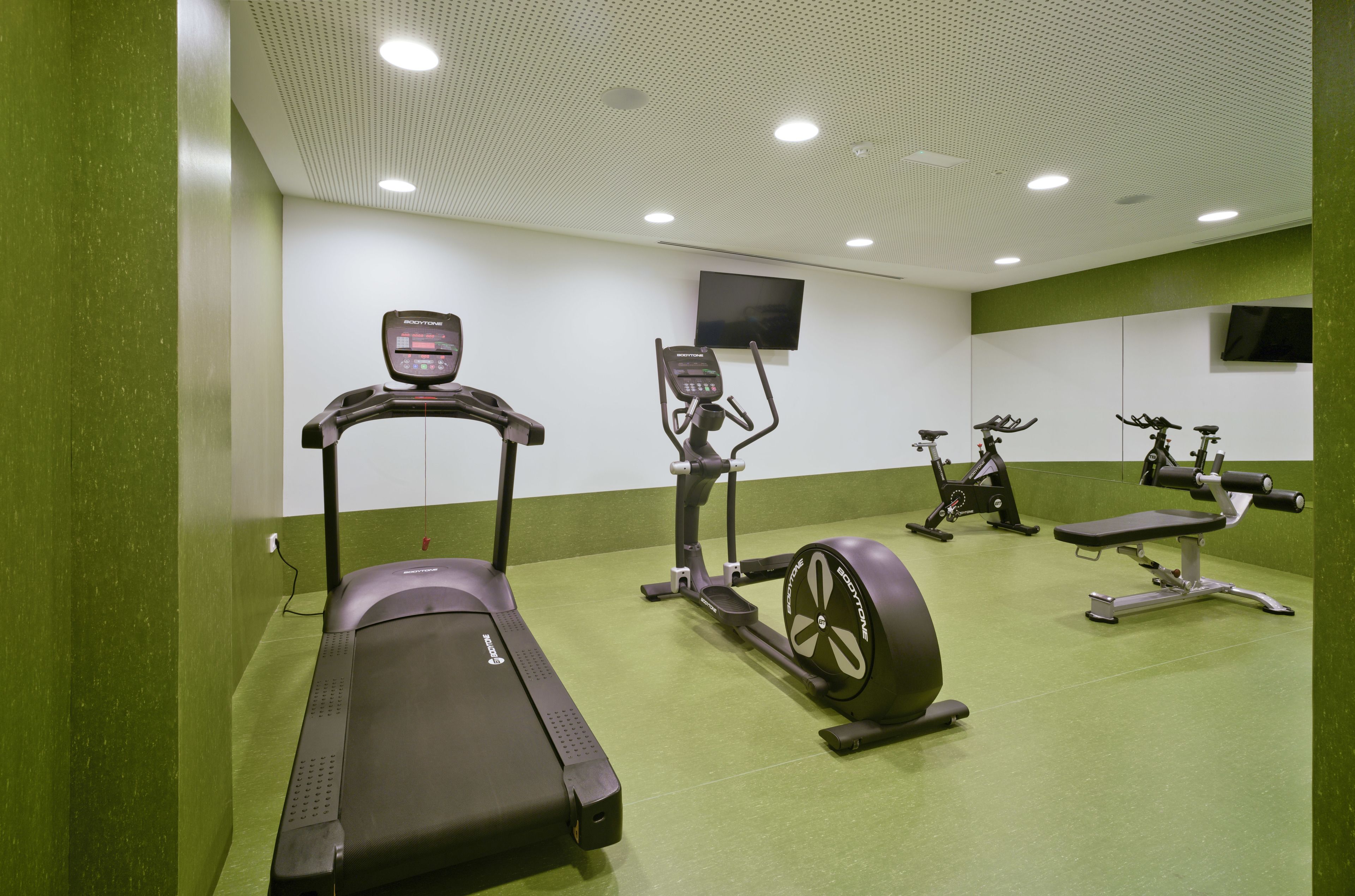 A gym with treadmills, elliptical machines, and a bench.