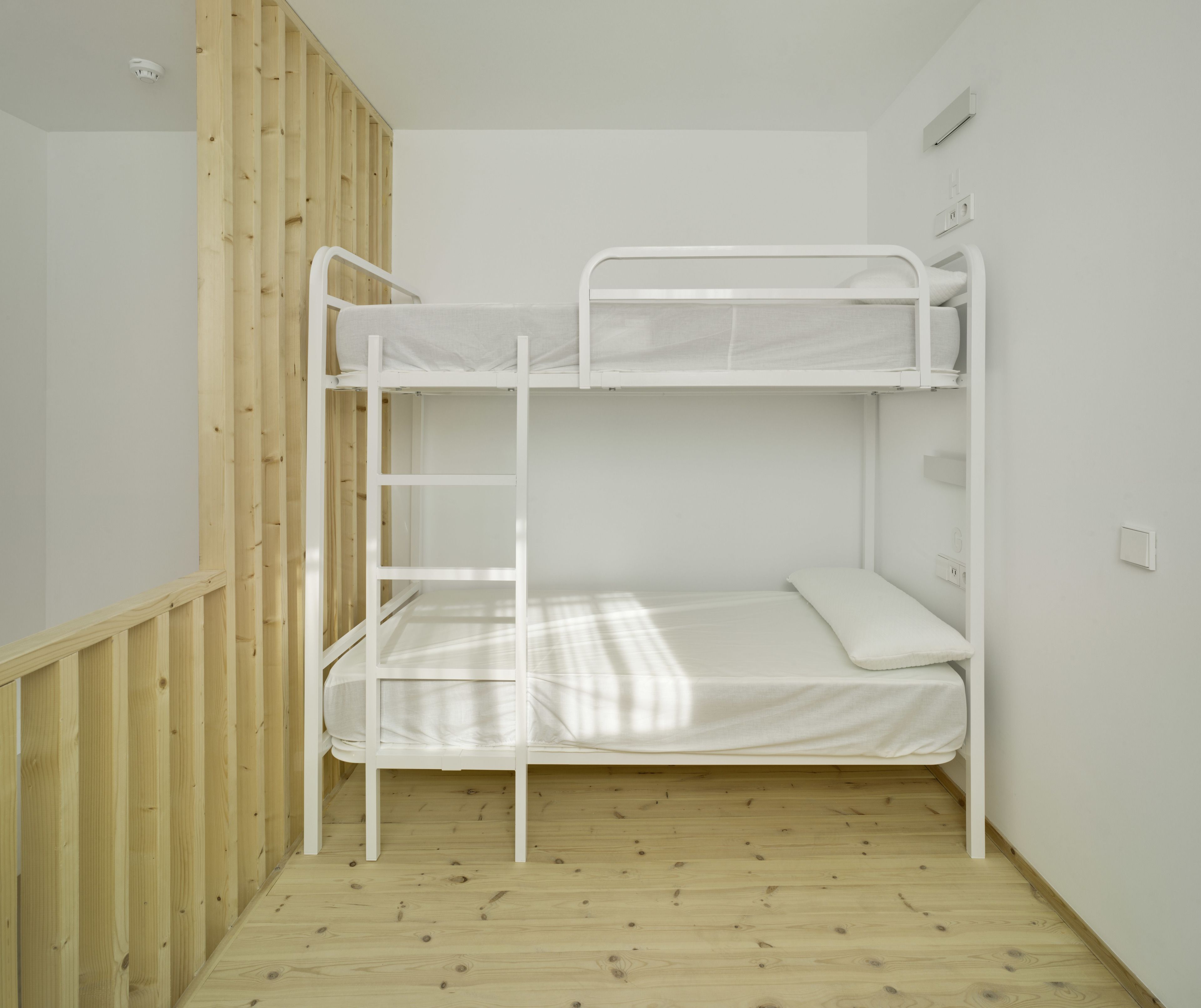 A bunk bed with a ladder, wooden floor, and white walls.
