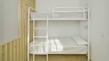 A bunk bed with a ladder, wooden floor, and white walls.