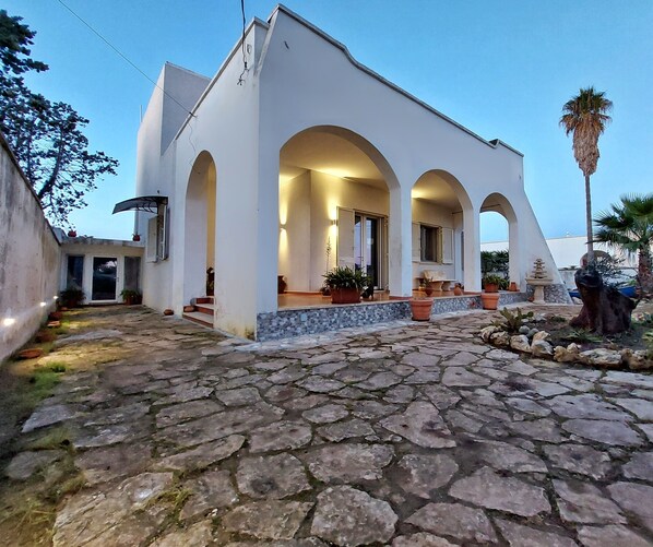 A modern building with a stone-paved courtyard, arched entryway, and potted plants. - Villa Musella (Porto Cesareo)