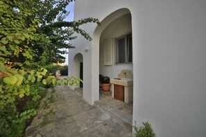 A stone-paved courtyard with white walls and arches, a sink, and a potted plant. - Villa Musella (Porto Cesareo)