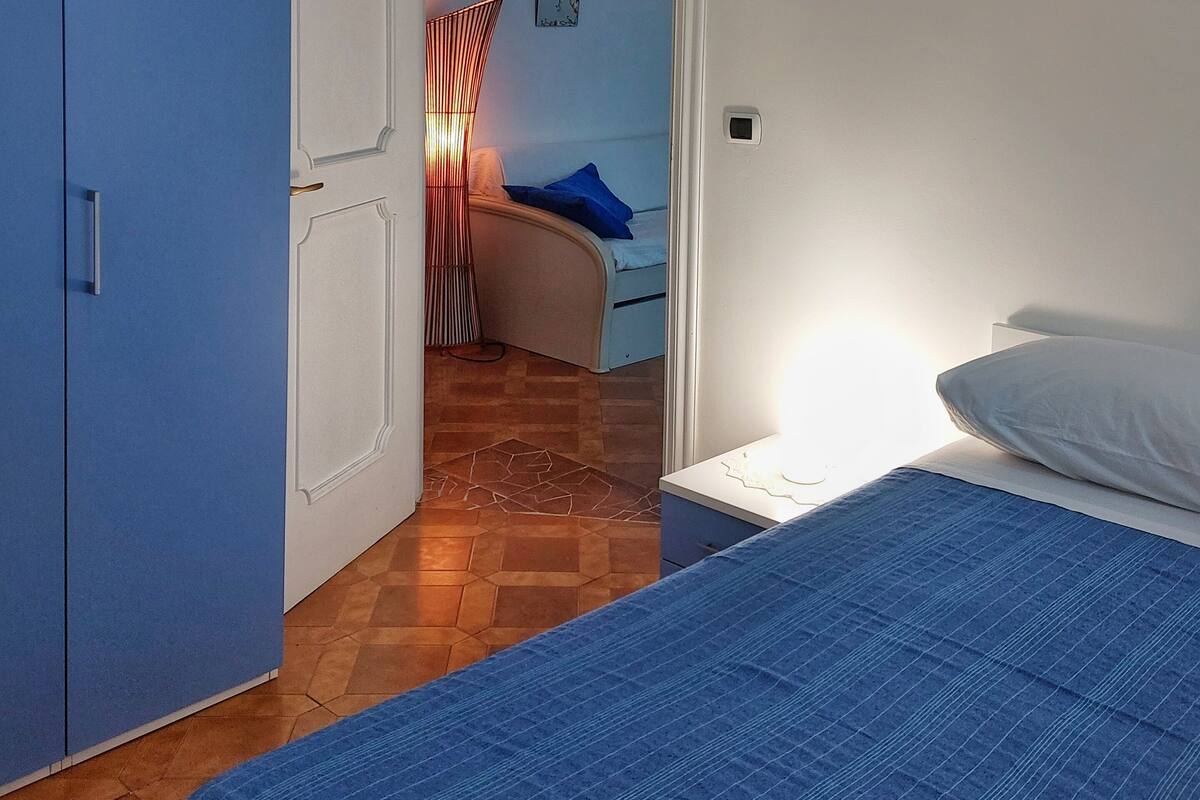 A bedroom with a bed, a nightstand, a blue wardrobe, and a door leading to another room.