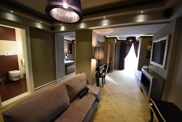 A hotel room with a sofa, a TV, a lamp, a piano, and a mirror. - Hymetis Palace (Pogradec)