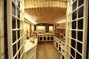 A narrow, brick-walled kitchen with white cabinets and a central island. - Hymetis Palace (Pogradec)