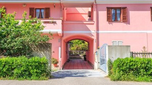 A pink building with an arched entrance, a gated driveway, and a small balcony with a potted plant. -  L'Aurora Viola (Carbonia)