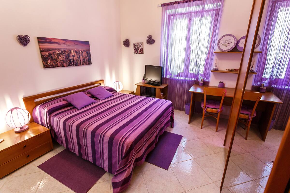 A bedroom with a bed, a desk, a chair, a TV, and decorative items on the walls.