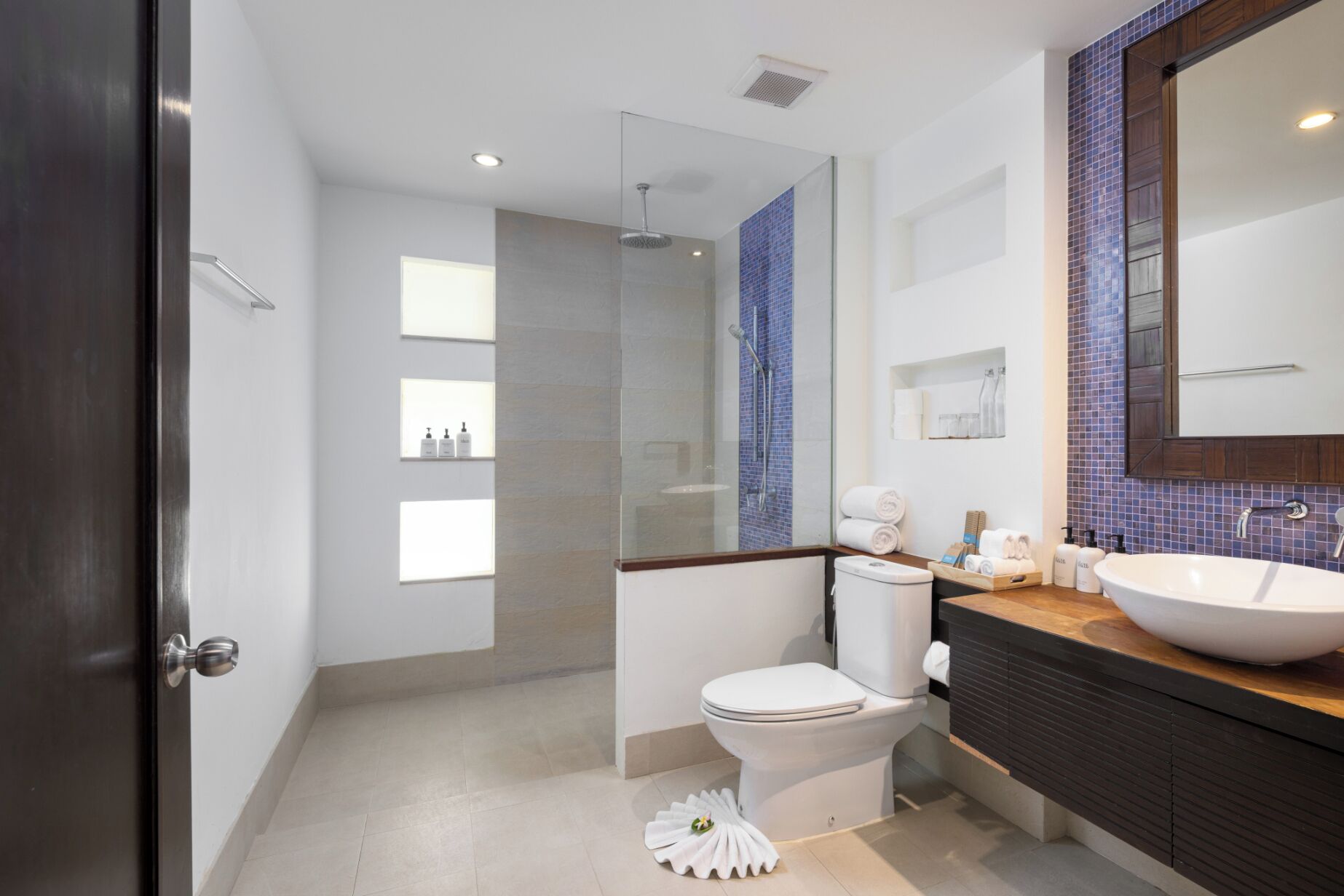 Ein modernes Badezimmer mit einer gläsernen Dusche, einer weißen Toilette, einem großen Waschbecken und einem Spiegel darüber.
