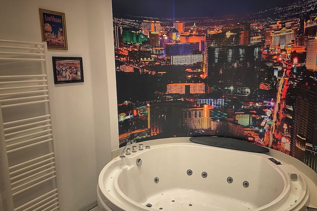 A bathroom with a large bathtub, a cityscape mural on the wall, and a framed picture of Las Vegas.