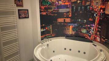 Une salle de bain avec une grande baignoire, une fresque murale représentant un paysage urbain et un tableau encadré de Las Vegas.