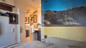 A bedroom with a bed, a bathroom with a sink and mirror, and a wall mural of mountains.