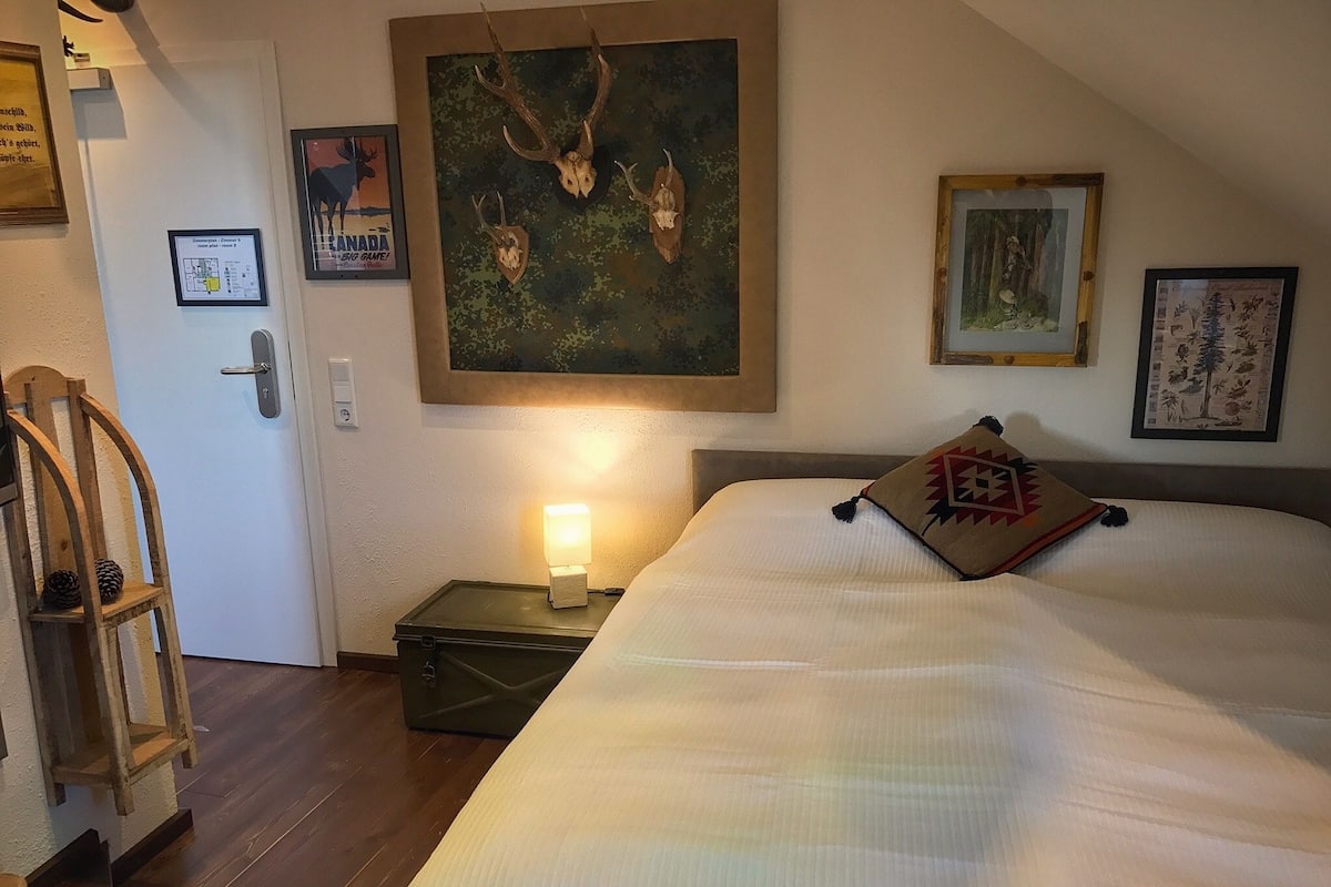 A hotel room with a large bed, a nightstand with a lamp, a wooden chair, and a door.