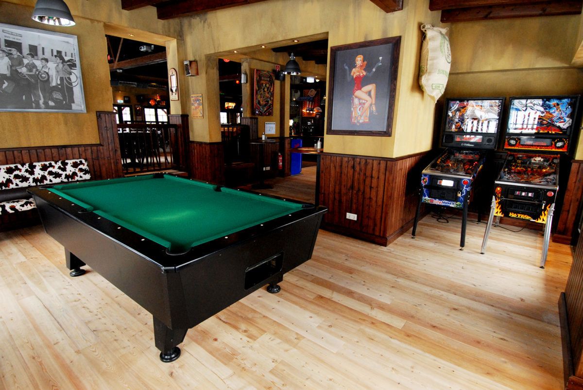 Sala de billar con mesa de billar, juegos de arcade y piso de madera.