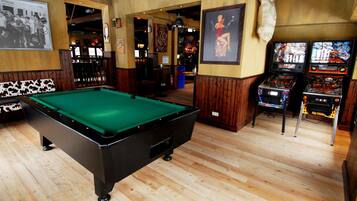 Sala de billar con mesa de billar, juegos de arcade y piso de madera.