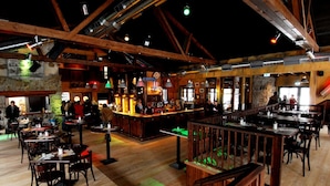 A spacious restaurant with high wooden ceilings, a bar area, and multiple dining tables and chairs.