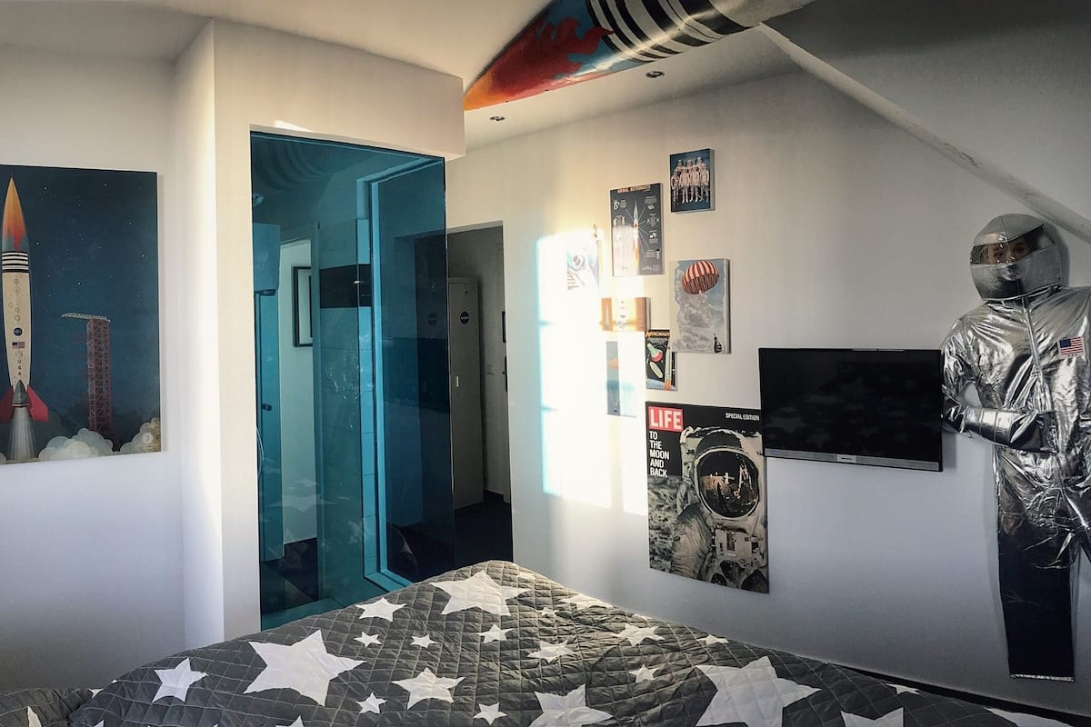 A bedroom with a bed featuring a star-patterned quilt, a poster of a rocket, and a life magazine on the wall.