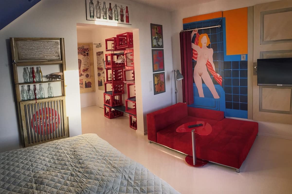 A room with a bed, a red sofa, a TV, and a red storage unit with shelves.