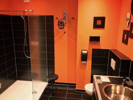 Un baño con azulejos negros y anaranjados, una ducha, un inodoro y un lavabo.