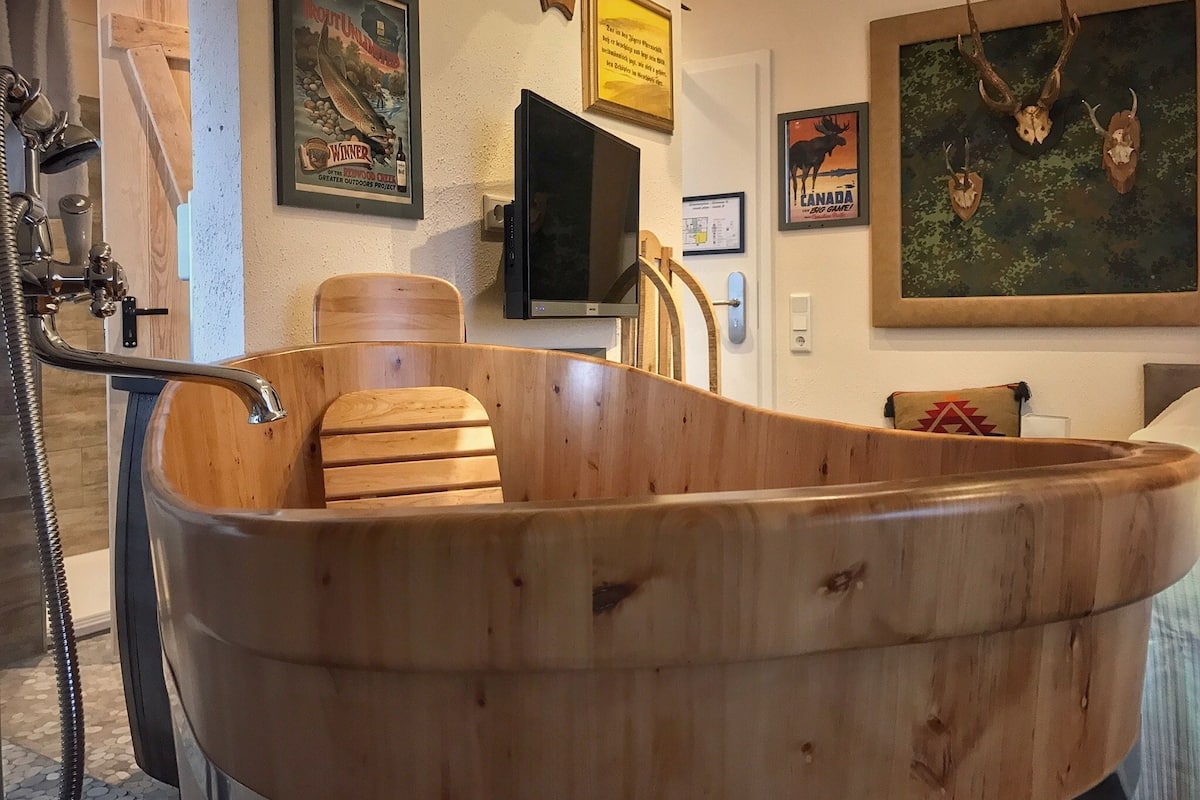 A wooden bathtub in a room with a television, framed pictures, and a mounted deer head.