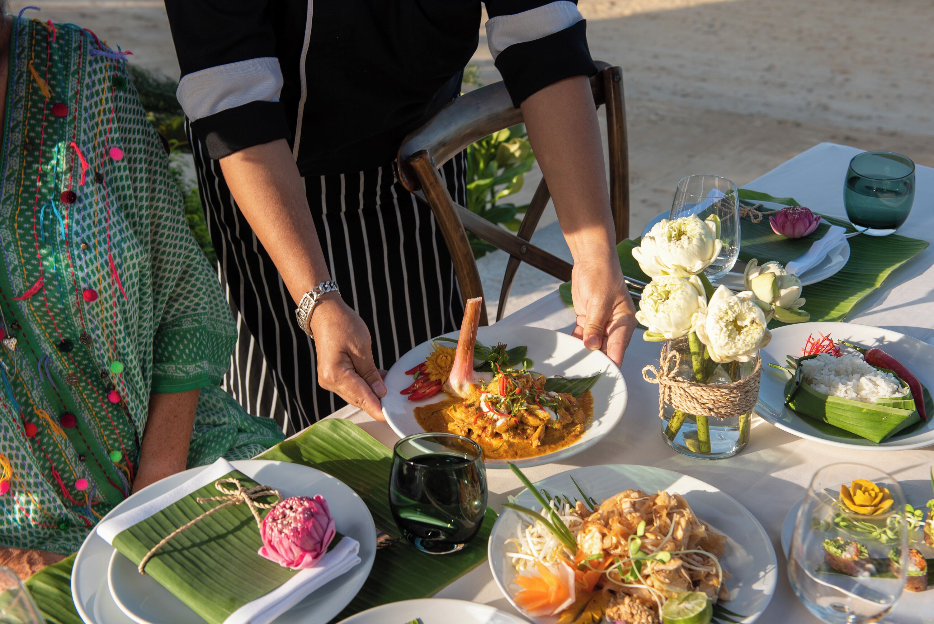 A table set with various dishes, including a plate with a flower arrangement, a bowl of rice, and a glass of dark liquid.
