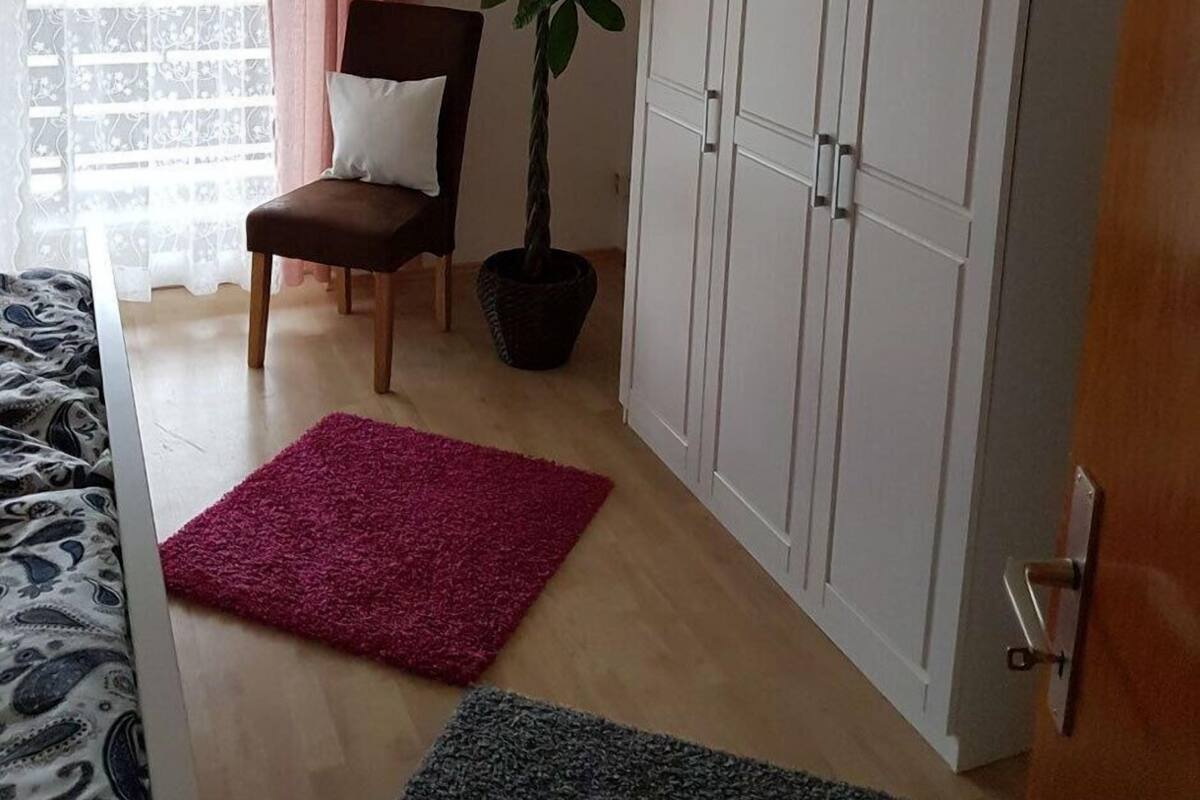 A room with a bed, a chair, a potted plant, a wardrobe, and a window with curtains.