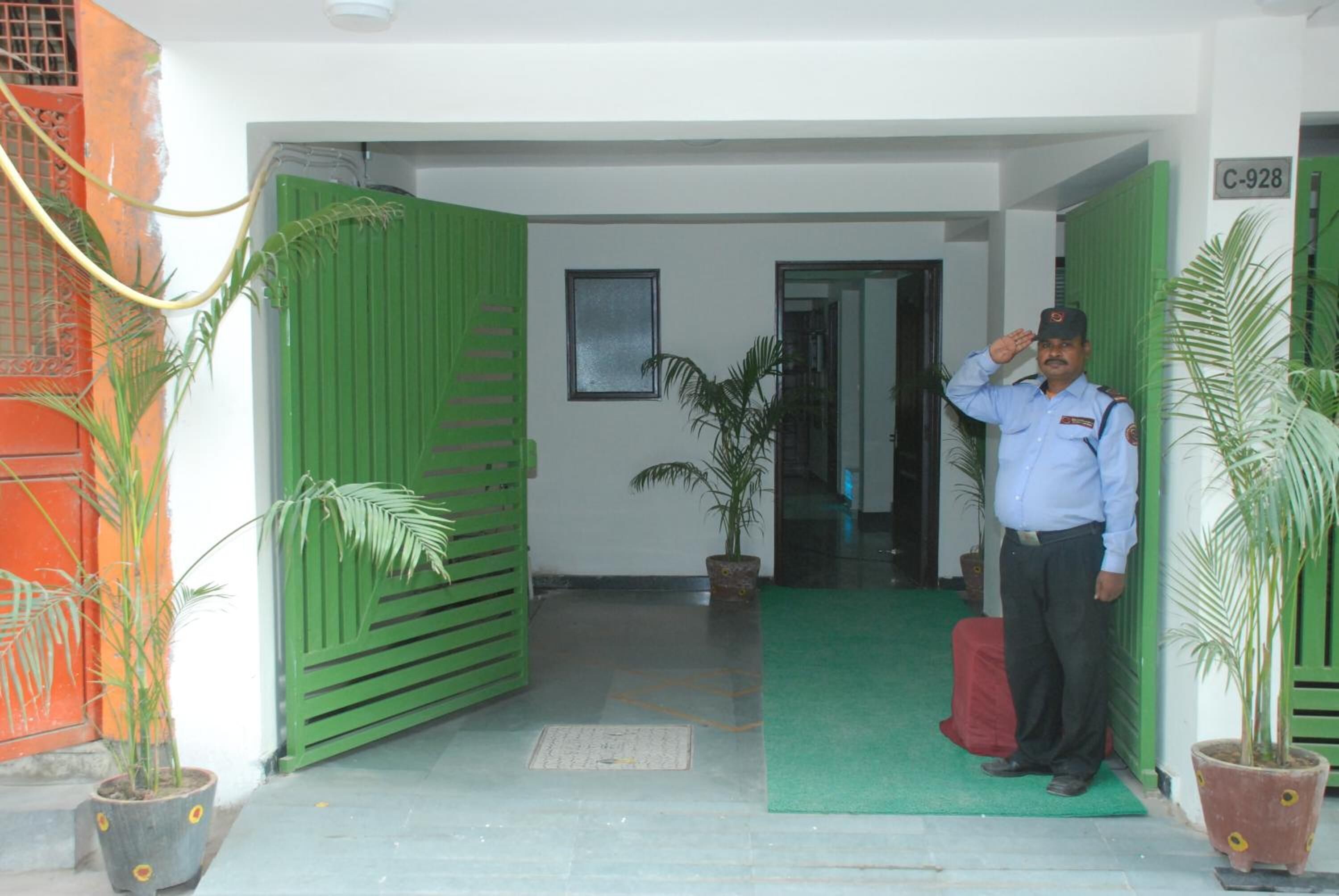 A man in uniform saluting at the entrance of a building with green doors and a green mat.