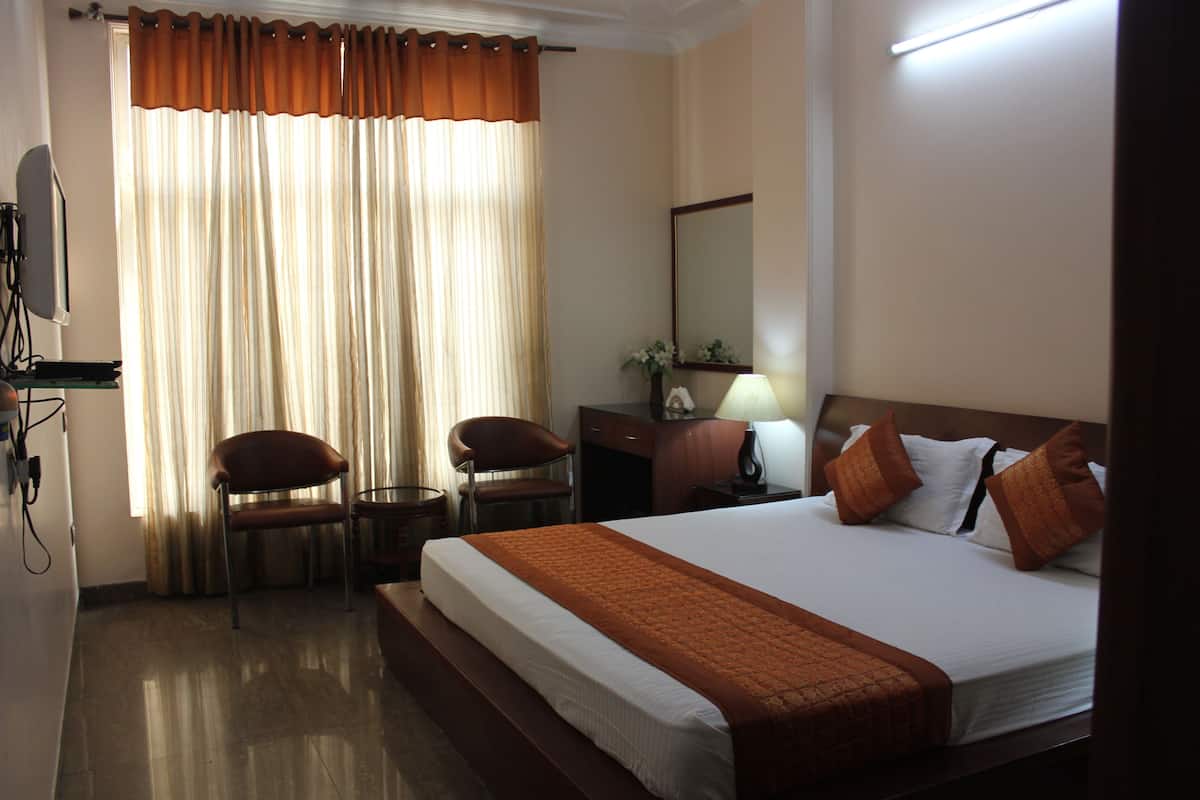 A hotel room with a large bed, two chairs, a desk, a lamp, and a mirror.