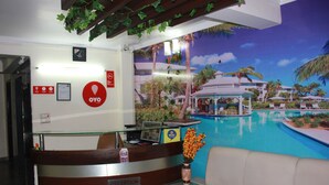 A reception area with a glass desk, a reception sign, and a view of a pool with palm trees. - Hotel Gokul Residency (New Delhi)