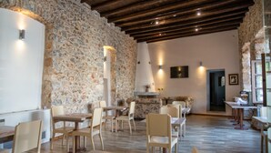 Un interior rústico con paredes de piedra, vigas de madera y una variedad de arreglos de asientos, incluyendo mesas y sillas.