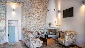 Una habitación acogedora con pared de piedra, chimenea, dos sillones estampados, una mesa de centro y un televisor montado en la pared.
