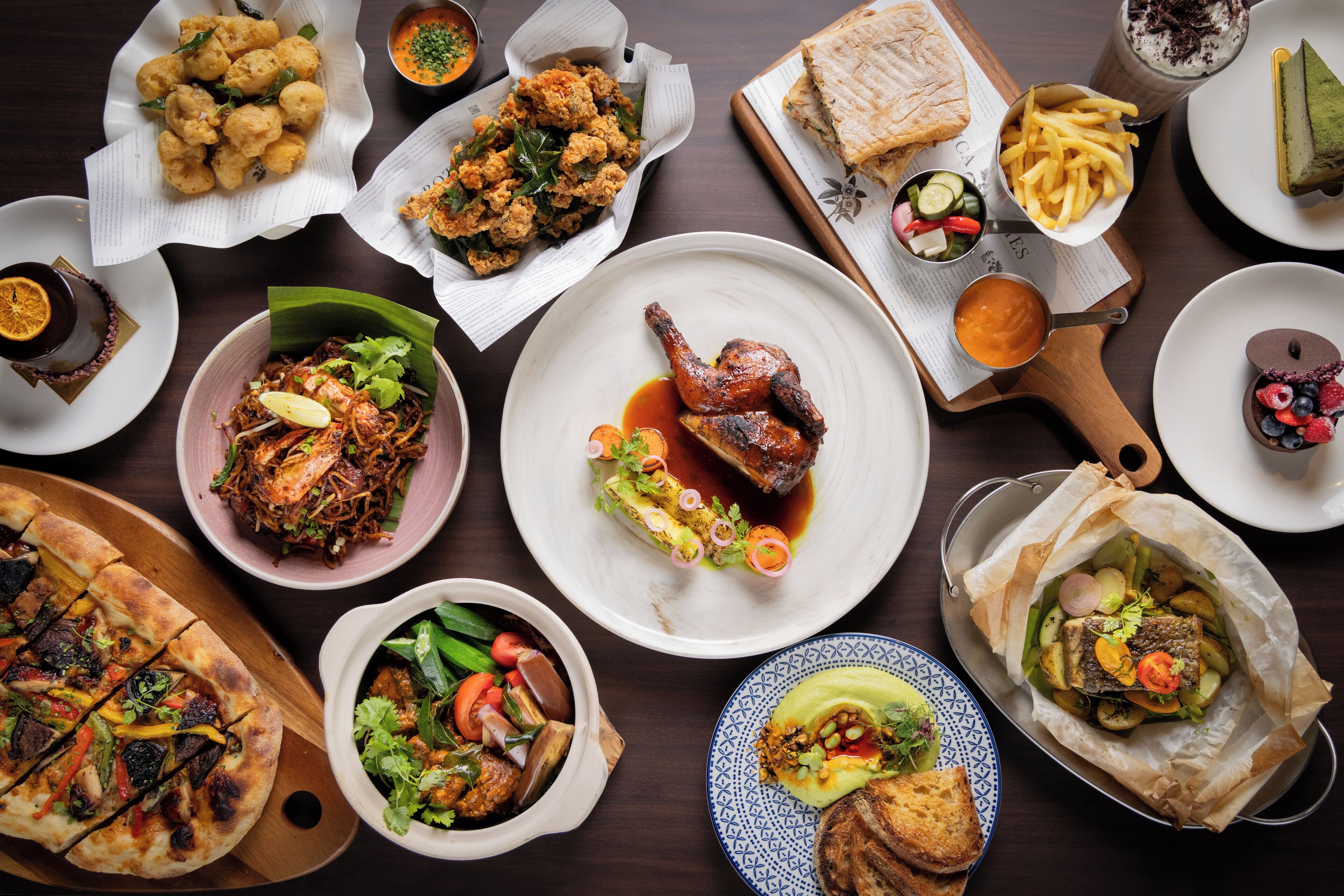 A variety of dishes including grilled meats, vegetables, and bread, arranged on a wooden table.