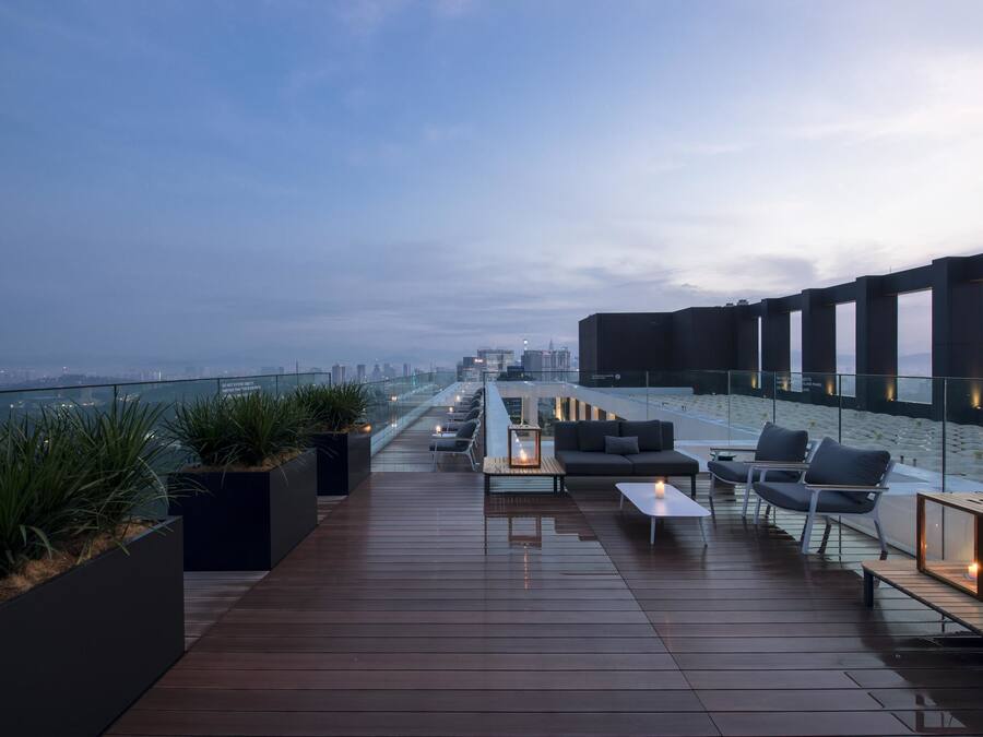 Una terraza en la azotea con vistas al horizonte de la ciudad, muebles modernos para exteriores y barandilla de cristal.