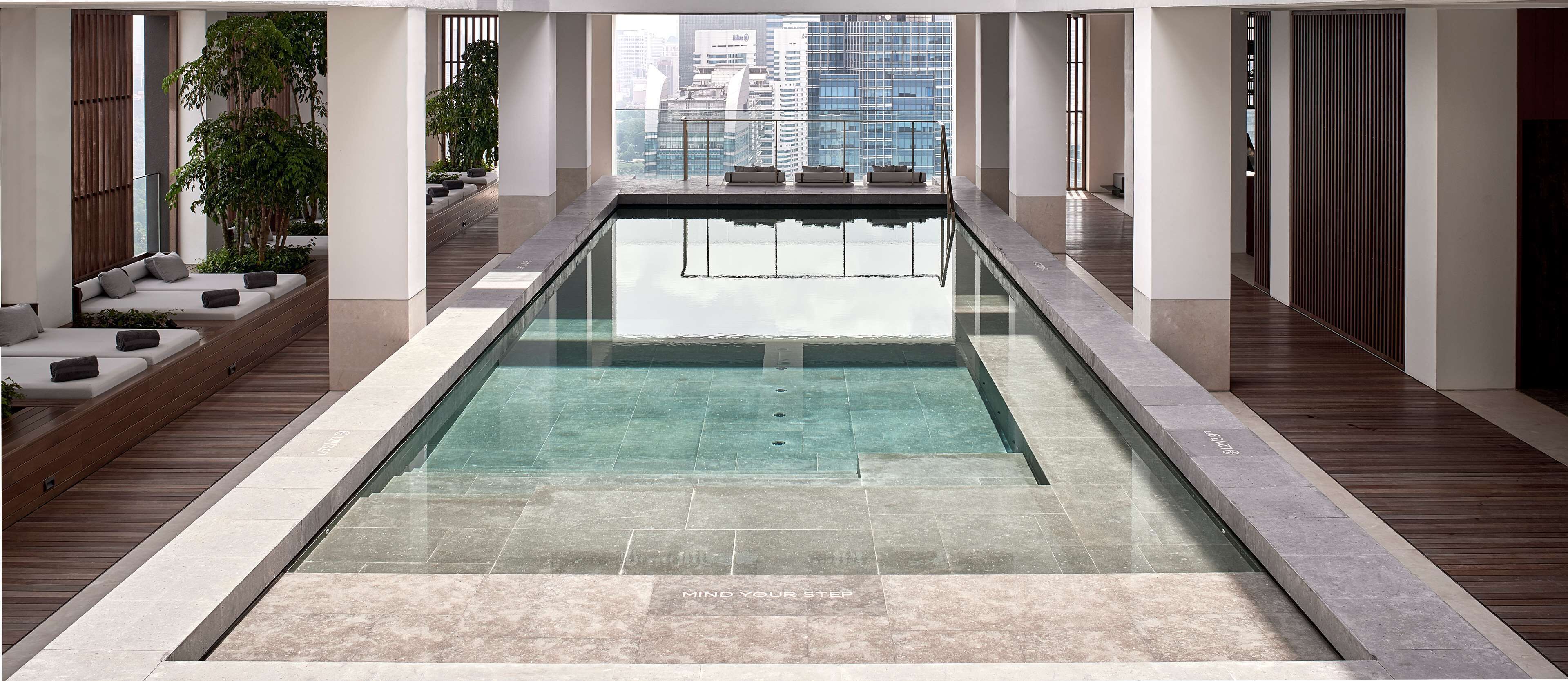 A modern indoor swimming pool with clear water, wooden deck, and seating areas.