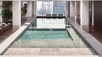 A modern indoor swimming pool with clear water, wooden deck, and seating areas.
