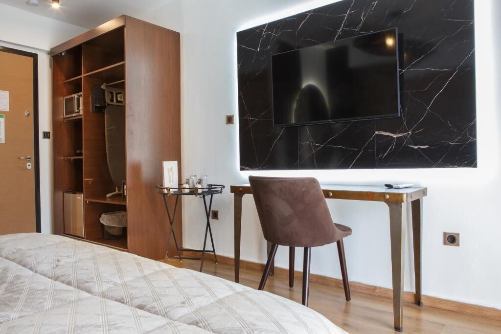 A bedroom with a bed, a desk with a chair, a TV mounted on a marble wall, and a wardrobe.