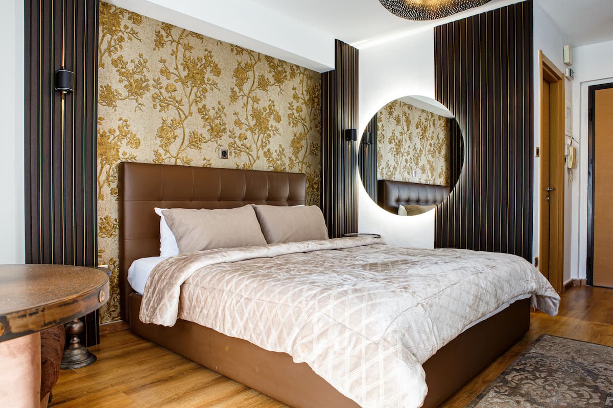 A bedroom with a large bed, a round mirror, a wooden floor, and a patterned wall.