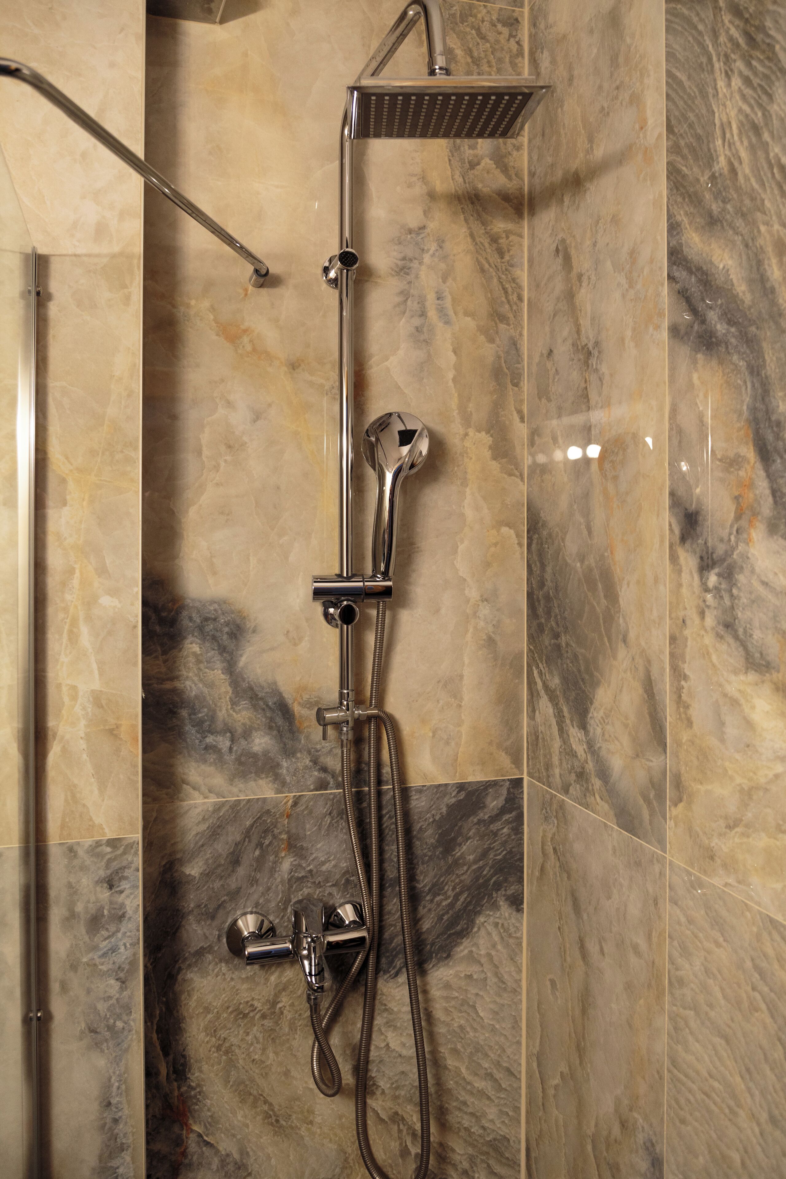 Une douche équipée d’un pommeau de douche à main, d’un pommeau de douche fixe et d’un flexible.